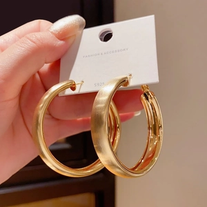Close-up of golden brushed metal hoop earrings with S925 silver needle on white card