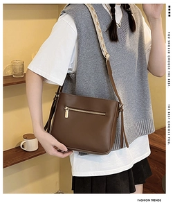 Detail of a dark brown leather crossbody bag featuring a vintage woven shoulder strap and golden zipper