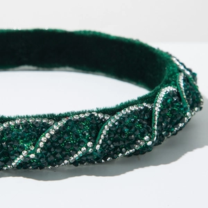 Dettaglio macro del cerchietto in velluto verde scuro con strass smeraldo scintillanti