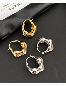 Gros plan de boucles d'oreilles irrégulières or et argent sur fond de cuir texturé