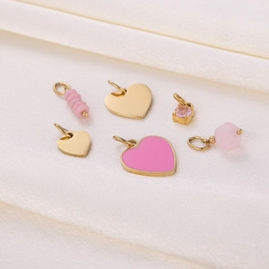 Flat lay of six gold stainless steel and pink enamel heart pendants on white silk