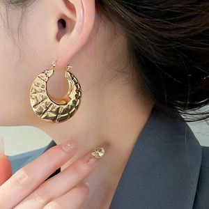 Close-up of large gold-finish textured hoop earrings on model with geometric pattern