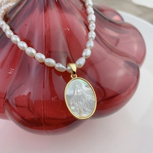 Macro view of freshwater pearl necklace with carved Virgin Mary shell pendant on glass