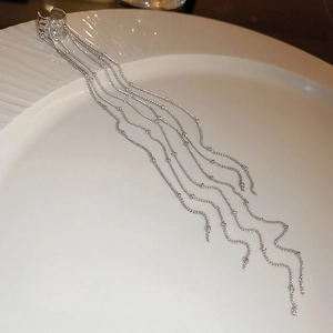 Detail of silver long tassel ear cuff with beaded metal chains on ceramic plate