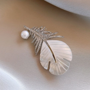 Detail of a 14k gold-plated feather brooch with pearls and shell inlay on silk fabric