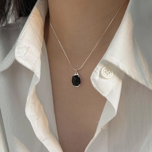 Close-up of elegant black oval agate pendant on silver snake chain worn on white shirt