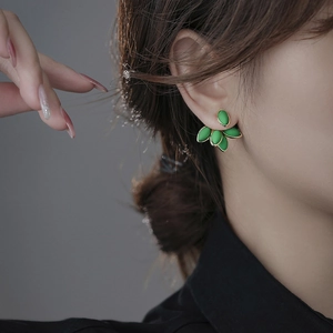 Detail view of vintage green leaf stud earrings with gold trim on model ear