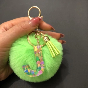 Detail of green fluffy pom pom keychain with resin letter J and colorful heart sequins