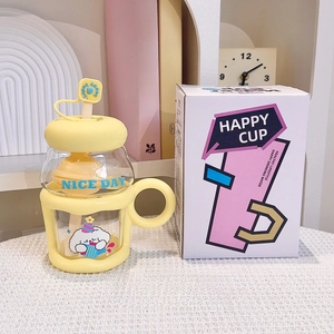 Close-up of yellow cartoon glass cup with straw handle and gift box on a desk
