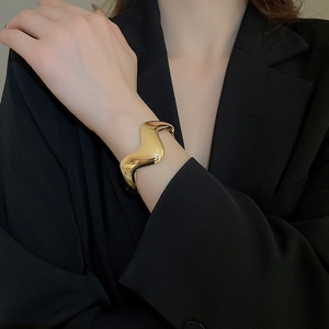 Detailed view of wide gold wave cuff bracelet on a black suit jacket sleeve
