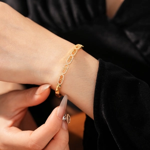 Close-up of gold oval bracelet with zircons on model's wrist against black velvet