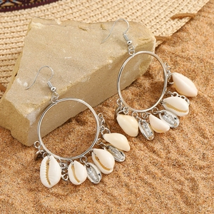 Silver hoop earrings with natural shells on rock with beach background