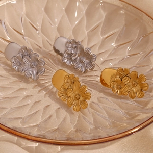 Detailed close-up of 18K gold and silver triple flower earrings on a glass plate