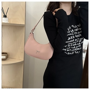 Pink crescent underarm bag with metal bow detail shown on shoulder with casual outfit