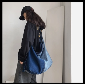 Detail view of large two-tone patchwork denim hobo bag worn by a model in a studio