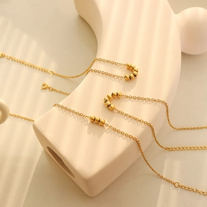 Elegant 18K gold plated beaded anklet hanging on a beige artistic stand in soft sunlight