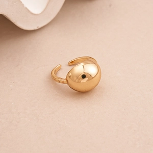 Polished gold bean-shaped open ring detail with high-gloss metallic finish on warm beige surface