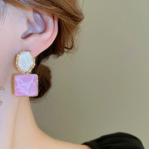 Nahaufnahme von quadratischen rosa Wellen-Ohrringen mit weißen Steinen an einem Model