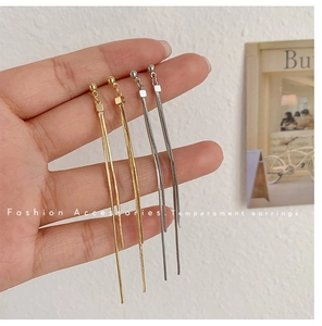 Detailansicht langer Quastenohrringe in Gold und Silber, präsentiert in der Hand