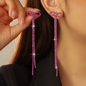Close-up of pink rhinestone bow drop earrings with long tassels on a model ear