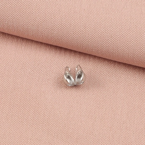 Macro view of silver double-hole crimp covers for DIY jewelry making on pink fabric