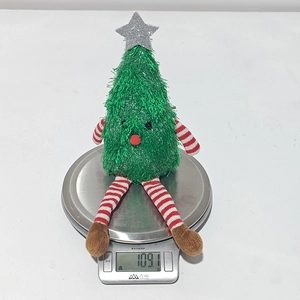 Weight display of a green plush Christmas tree doll with red striped legs on a scale