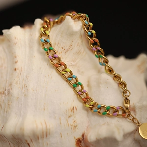 Detail of gold-plated lucky coin bracelet with colorful enamel links on a white seashell