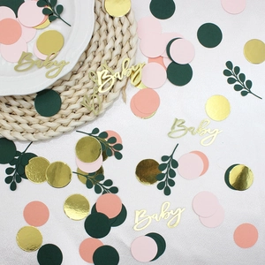 Nahaufnahme von Babyparty-Konfetti mit Goldbuchstaben, grünen Blättern und rosa Kreisen