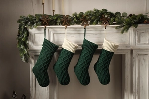Vier dunkelgrüne Strick-Weihnachtssocken mit weißem Rand hängend an einem Kaminmantel