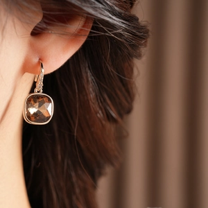 Gros plan d'une boucle d'oreille dorée avec pierre carrée marron et détails en zircon