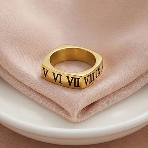Détail d'une bague carrée dorée avec gravures de chiffres romains noirs sur fond de soie