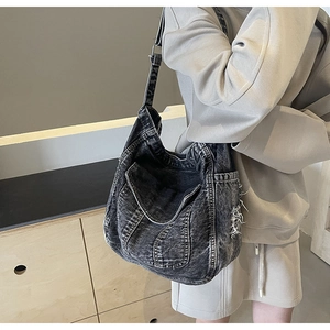 Détail d'un grand sac cabas en jean gris foncé avec bords effilochés porté par le mannequin