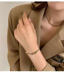 Close-up of golden necklace and bracelet set with colorful zircon stones on a model