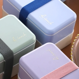 Close-up of three lunch boxes in blue, green, and pink with elastic straps and Hi-Lunch design