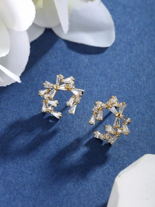 Close-up of gold flower stud earrings with sparkling cubic zirconia on blue background