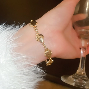 Elegant gold shell link bracelet worn on wrist while holding a wine glass against dark tones