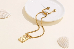 Detailed macro view of golden square pendant and heart clasp on an elegant metal bracelet