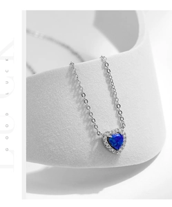 Détail du collier cœur avec pendentif opale bleue et zircons sur un support créatif blanc