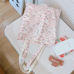 Detail view of pink floral canvas tote bag with wide handles and brand label on white desk