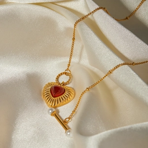 Detail of 18k gold plated heart necklace with red agate stone on white silk background