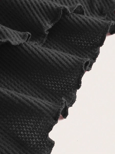Detail shot of black waffle knit fabric texture and elegant ruffled edge craftsmanship