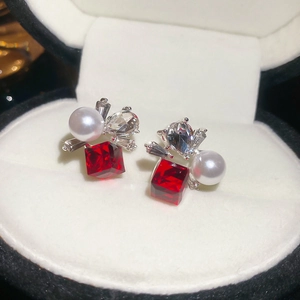 Macro shot of silver stud earrings with red square crystal and pearl on white velvet box