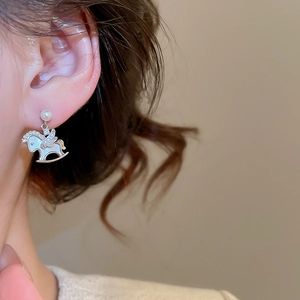 Close-up of pearl stud earring with a silver rocking horse pendant and shell inlay
