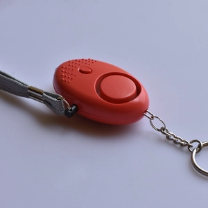 Detail view of red personal safety alarm with textured surface and silver keychain