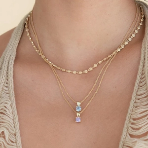 Close-up of layered gold S925 silver necklaces with blue and purple birthstone pendants