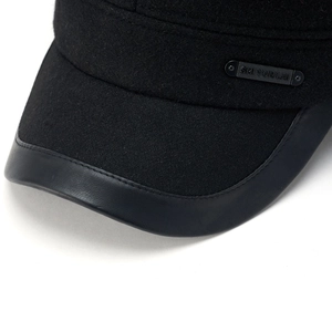 Macro detail of winter wool flat cap featuring leather piping and metal logo plate