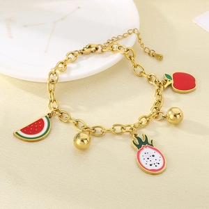 Detail of 18K gold stainless steel bracelet with colorful enamel fruit charms on warm background