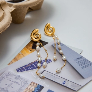 Detail of gold spiral earrings with white baroque pearl tassels on editorial background