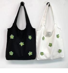 Detail of black and white canvas tote bags featuring 3D green knitted flower decorations