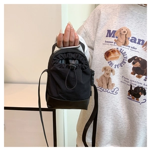 Detail of a black mini drawstring crossbody bag featuring canvas and leather stitching